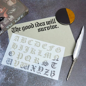 Pochoir alphabet gothique posé sur carte avec plume calligraphique pour scrapbooking littéraire