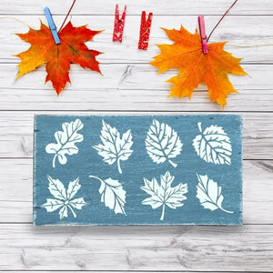 Pochoir feuille chêne peint blanc sur planche bleue, feuilles érables fixées par pinces