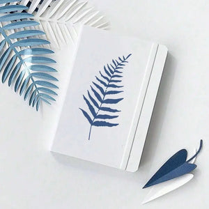 Pochoir imperméable feuille de fougère bleue sur carnet blanc, palme décorative à côté
