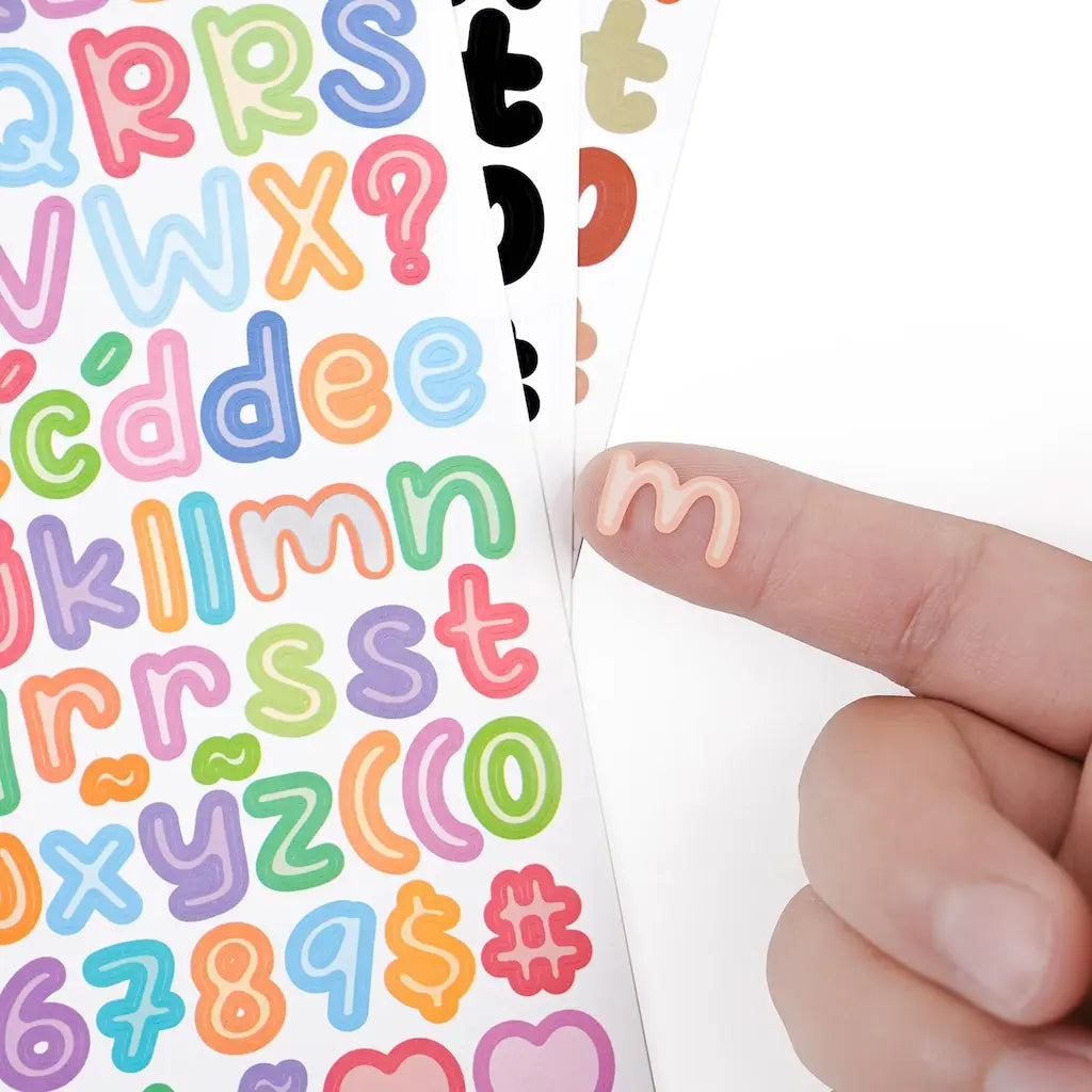 Stickers alphabet scrapbooking, palette classique noir, blanc et doré, vue d'un autocollant sur le doigt