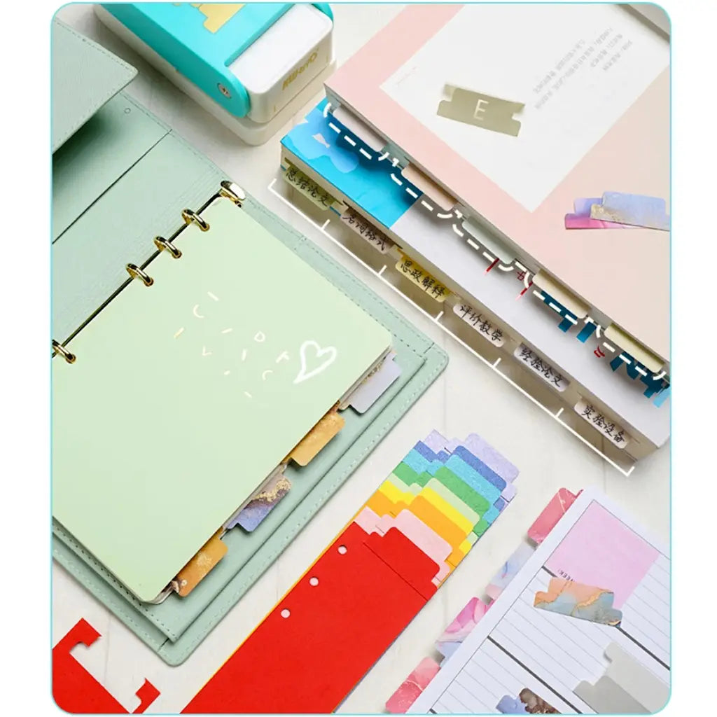 Perforatrice onglet scrapbooking blanche posée sur un agenda à anneaux et intercalaires colorés