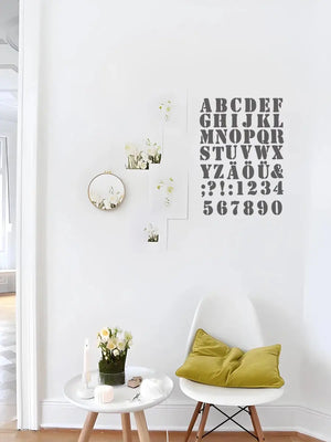Pochoir alphabet en grand lettrage mural gris dans un salon lumineux avec chaise jaune