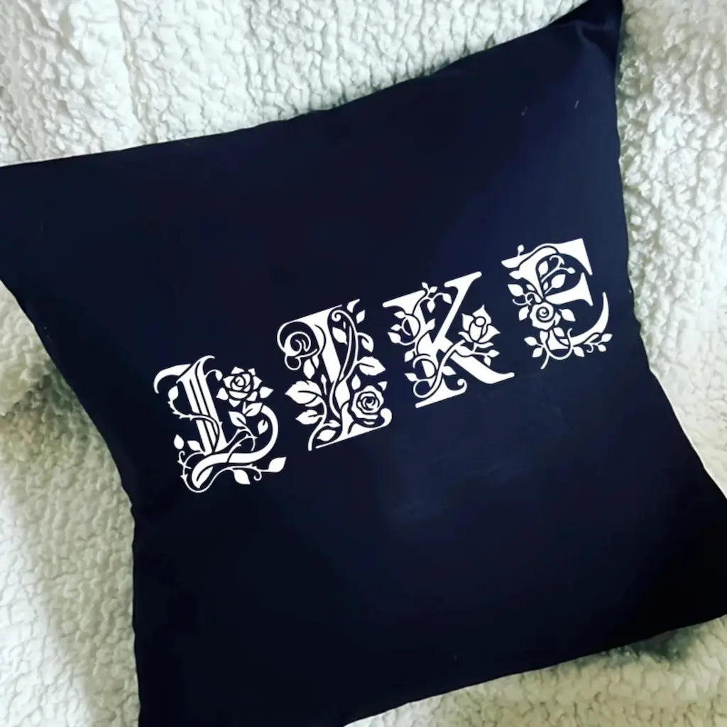 Pochoir alphabet floral LIKE peint blanc sur coussin bleu marine, lettres ornées roses feuillage