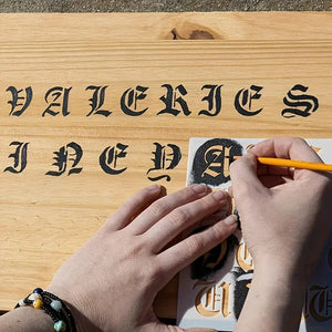 Pochoir alphabet gothique en cours d'application, lettres Valeries peintes sur planche bois