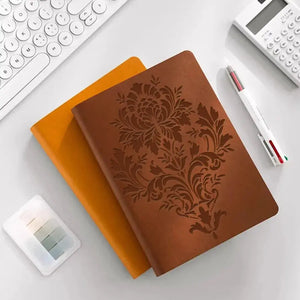 Carnet cuir brun gravé d'un motif pochoir baroque centré, posé sur bureau blanc