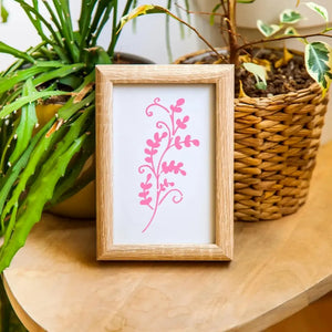 Pochoir dessin enfant motif fougère rose dans cadre bois, posé près de plantes vertes