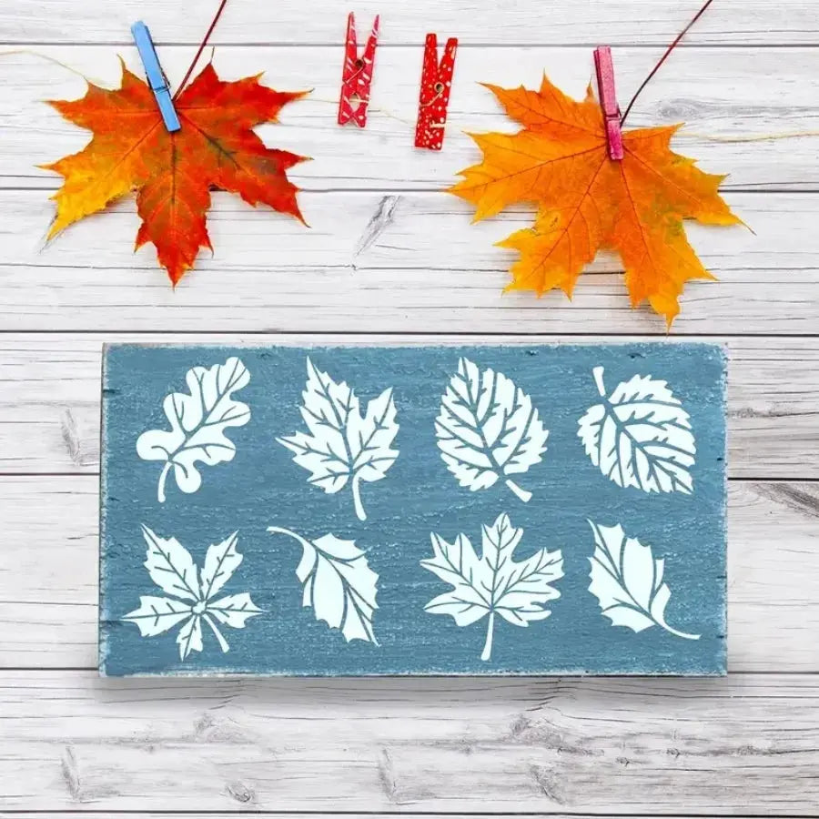 Pochoir feuille chêne peint blanc sur planche bleue, feuilles érables fixées par pinces