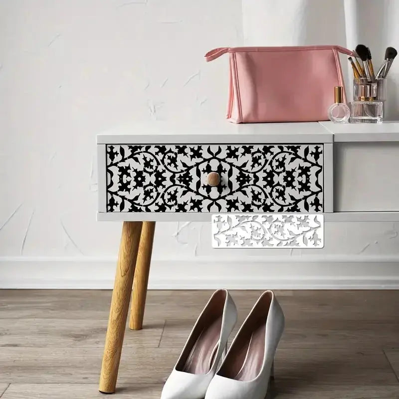 Pochoir frise florale appliqué noir sur tiroir blanc, escarpins et trousse rose à côté