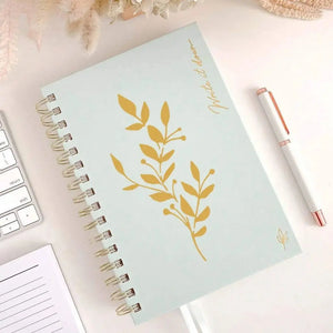 Pochoir imperméable feuillage doré sur carnet spirale menthe, stylo rose en accent