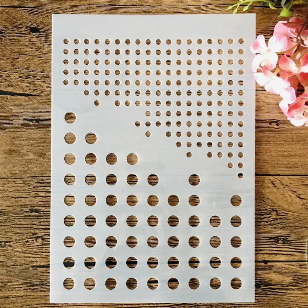 Pochoir pois multi-tailles graduées, motif points ronds répétés en plastique blanc fond bois