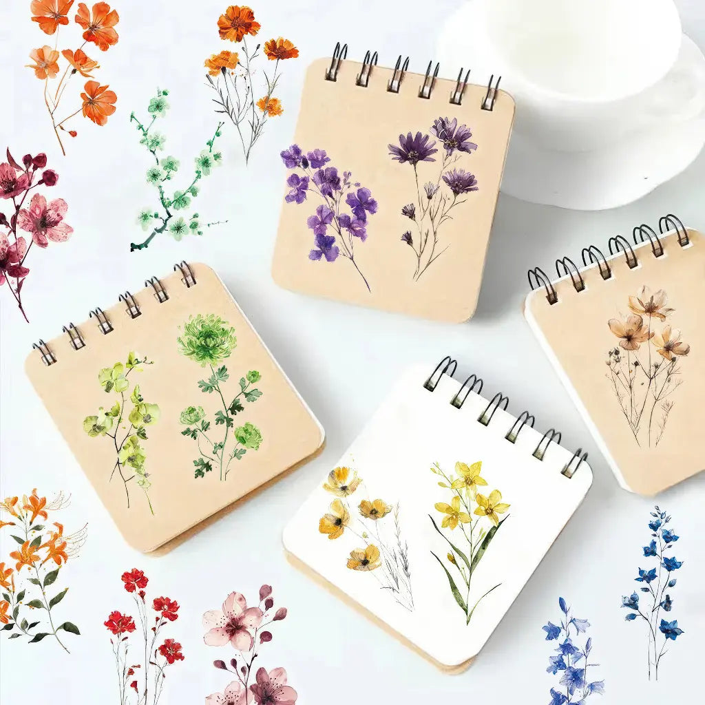 Stickers scrapbooking fleurs aquarelle posés sur des carnets à spirale, motifs violets, verts et jaunes